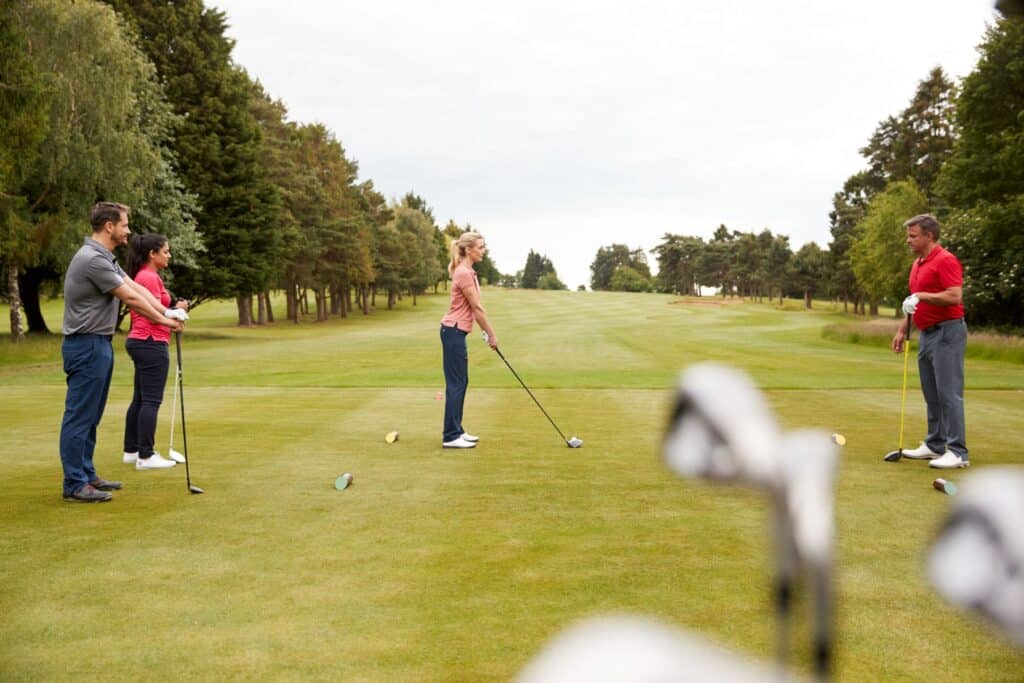 Golfprofi demonstriert Golfschlag auf dem Fairway für eine Gruppe von Golfern während des Unterrichts